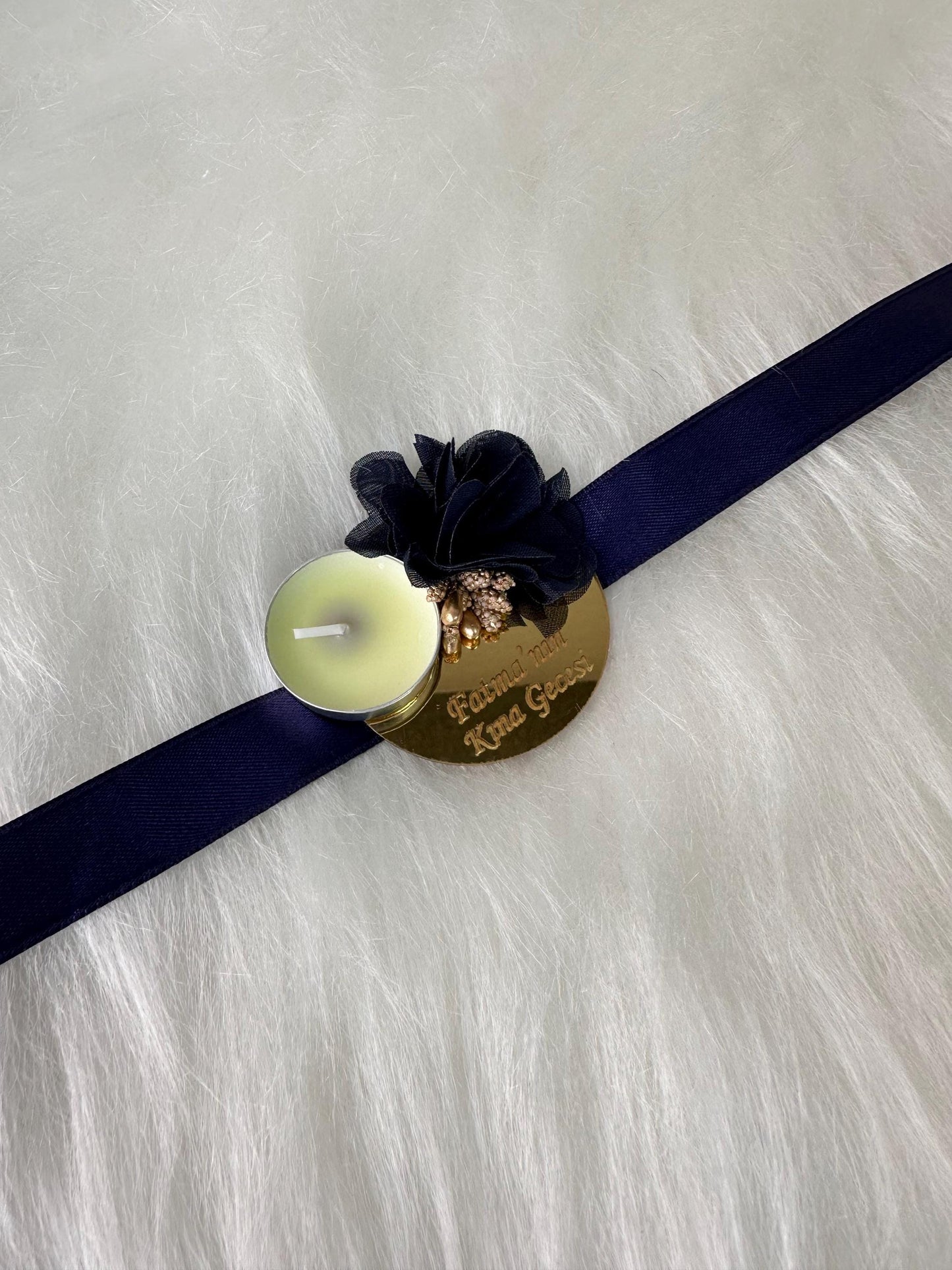 A gold round plaque with a black flower and a small white tea light candle. The plaque has the text