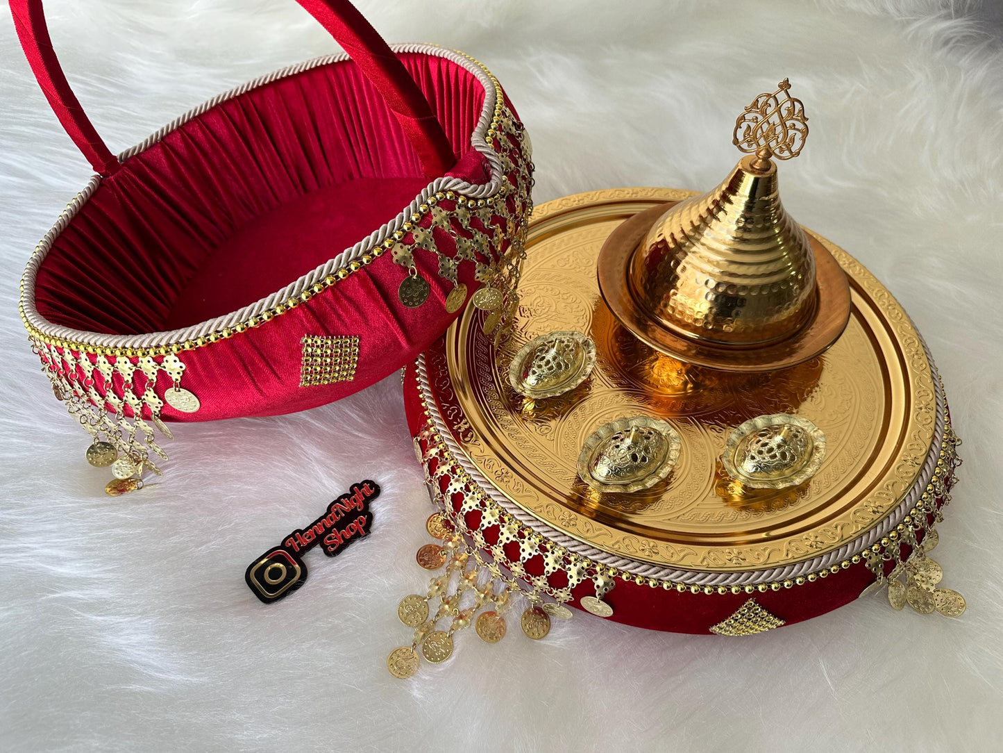 henna A red velvet tray with gold trim and gold coins hanging from the edge. The tray is filled with gold coins. A gold metal tray with a gold lid and three gold bowls is sitting on top of the red tray.