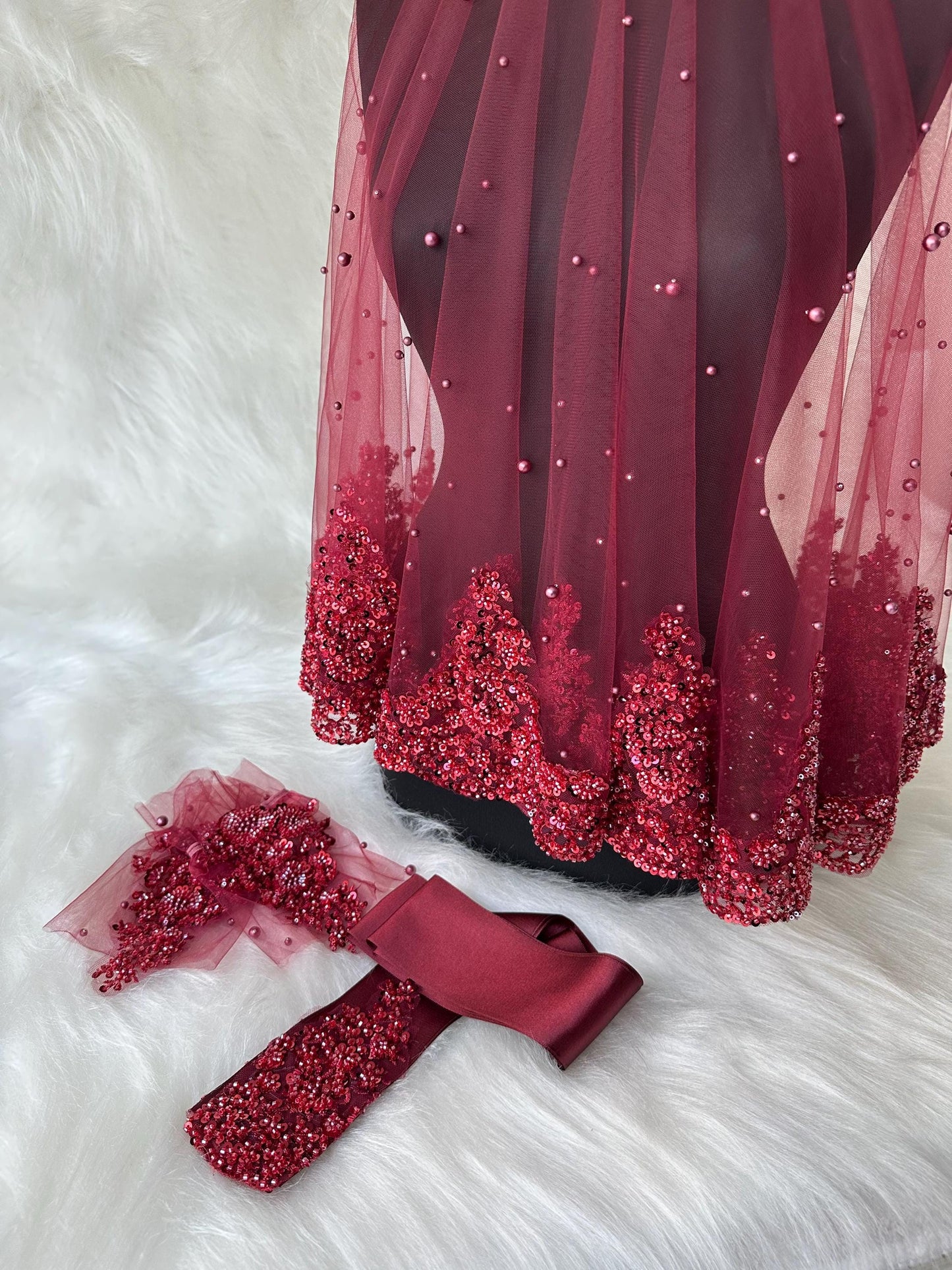 A burgundy tulle veil with pearl embellishments and a matching burgundy satin ribbon.