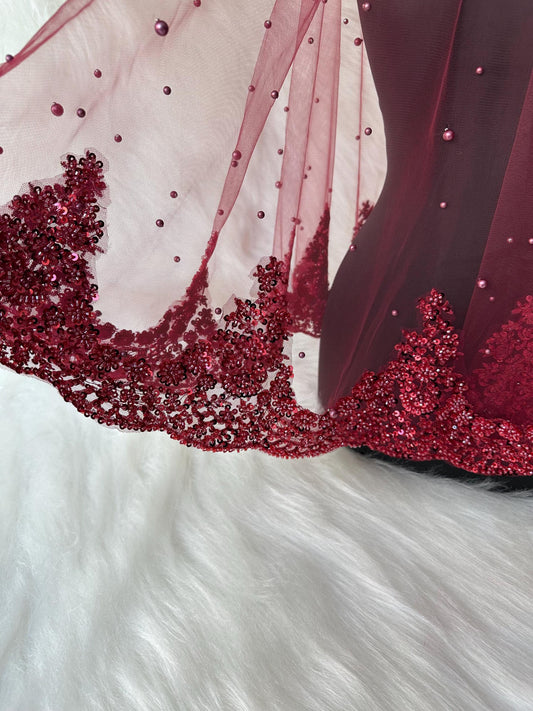 A burgundy sheer fabric with a beaded trim and sequins. The fabric is draped over a white surface.