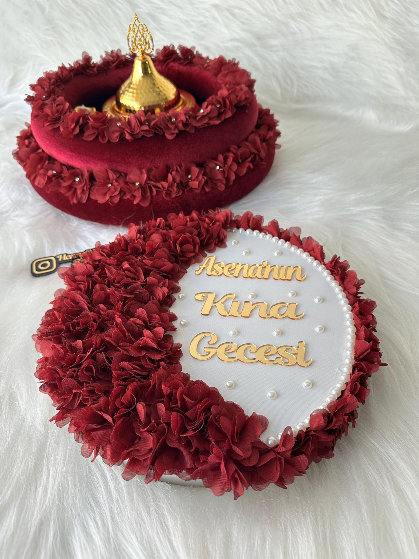 A white round tray with a red fabric trim. The tray has a gold inscription that reads 'Asenat'nin Kına Gecesi' and is decorated with white pearl beads.