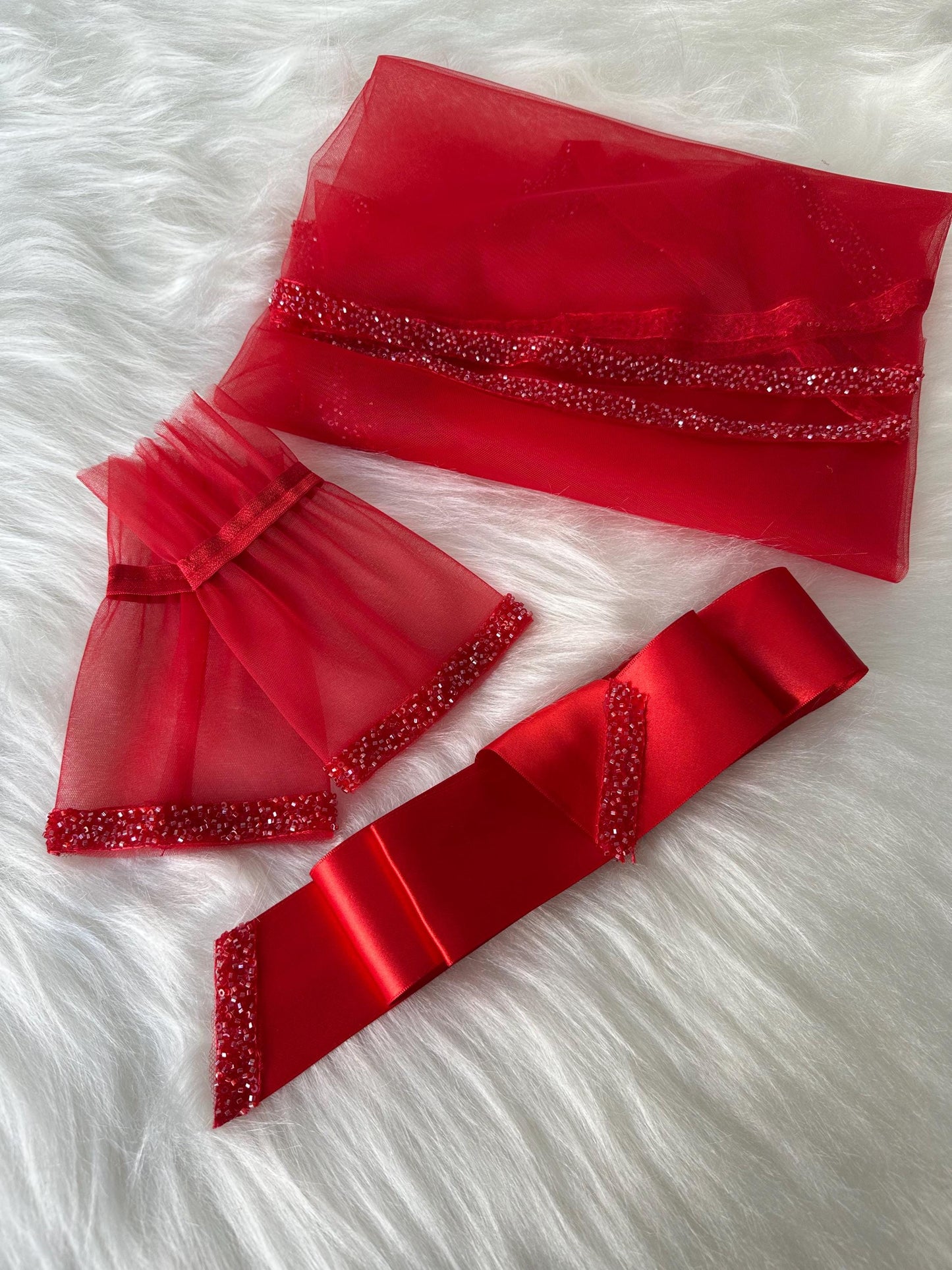 Red tulle fabric with beaded trim, a red satin ribbon with beaded trim, and two red tulle fabric wrist cuffs with beaded trim.