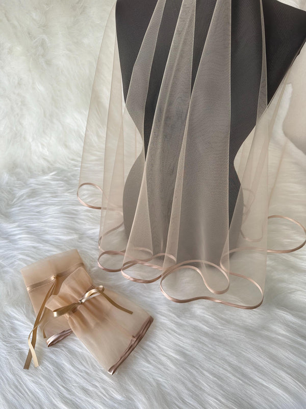 Two beige tulle veils with a satin trim. One veil is folded and tied with a ribbon. The other veil is draped over a mannequin.