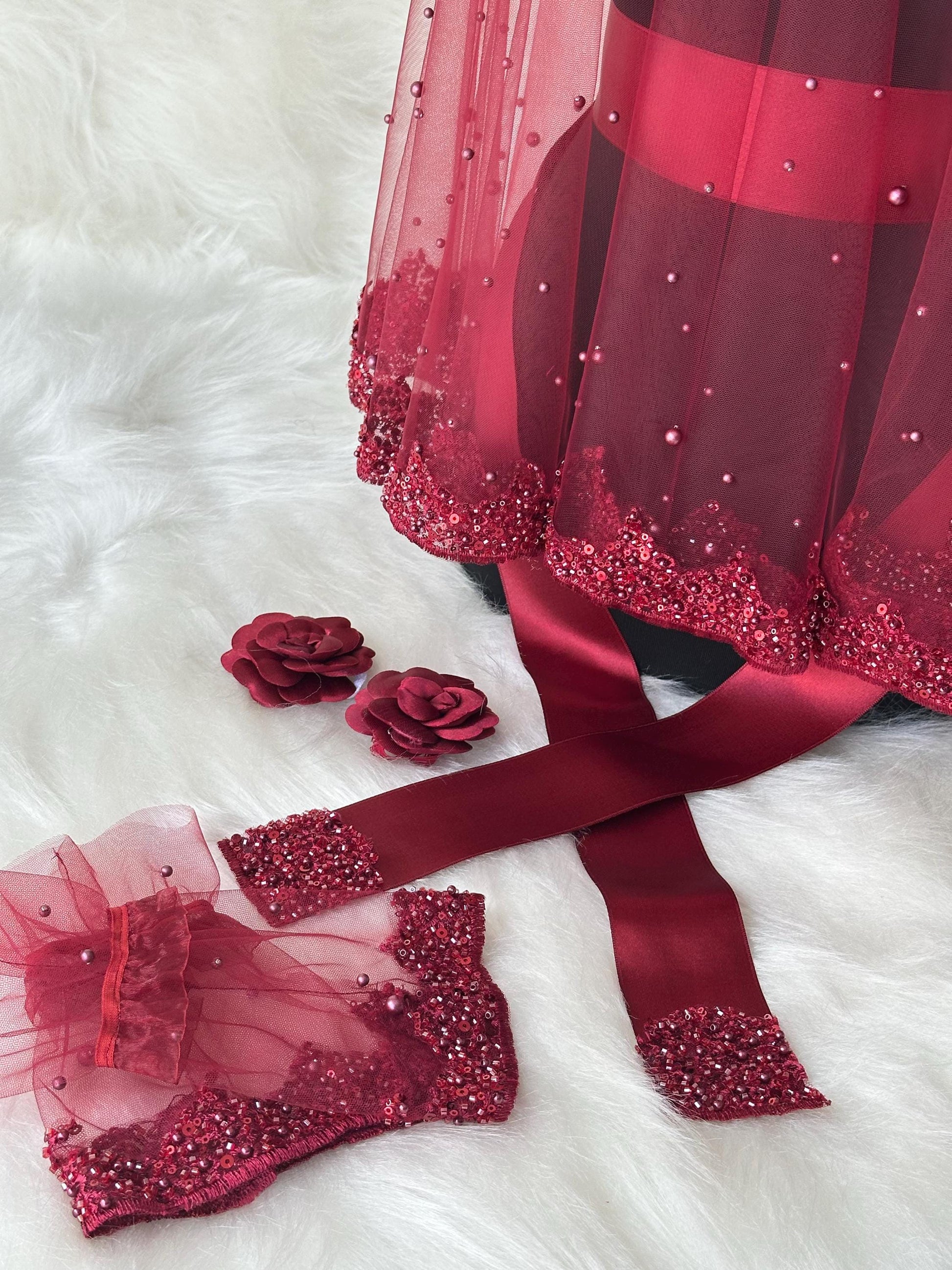 A burgundy tulle bridal veil with pearl embellishments, a matching burgundy satin ribbon, and two burgundy rose-shaped hair clips.