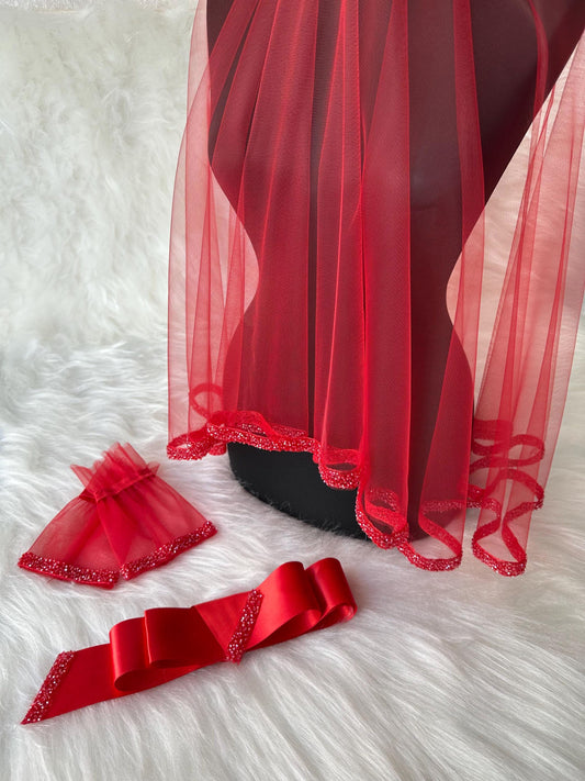 A red bridal veil with a beaded trim, a red satin sash with a beaded trim, and a red tulle wristlet with a beaded trim.
