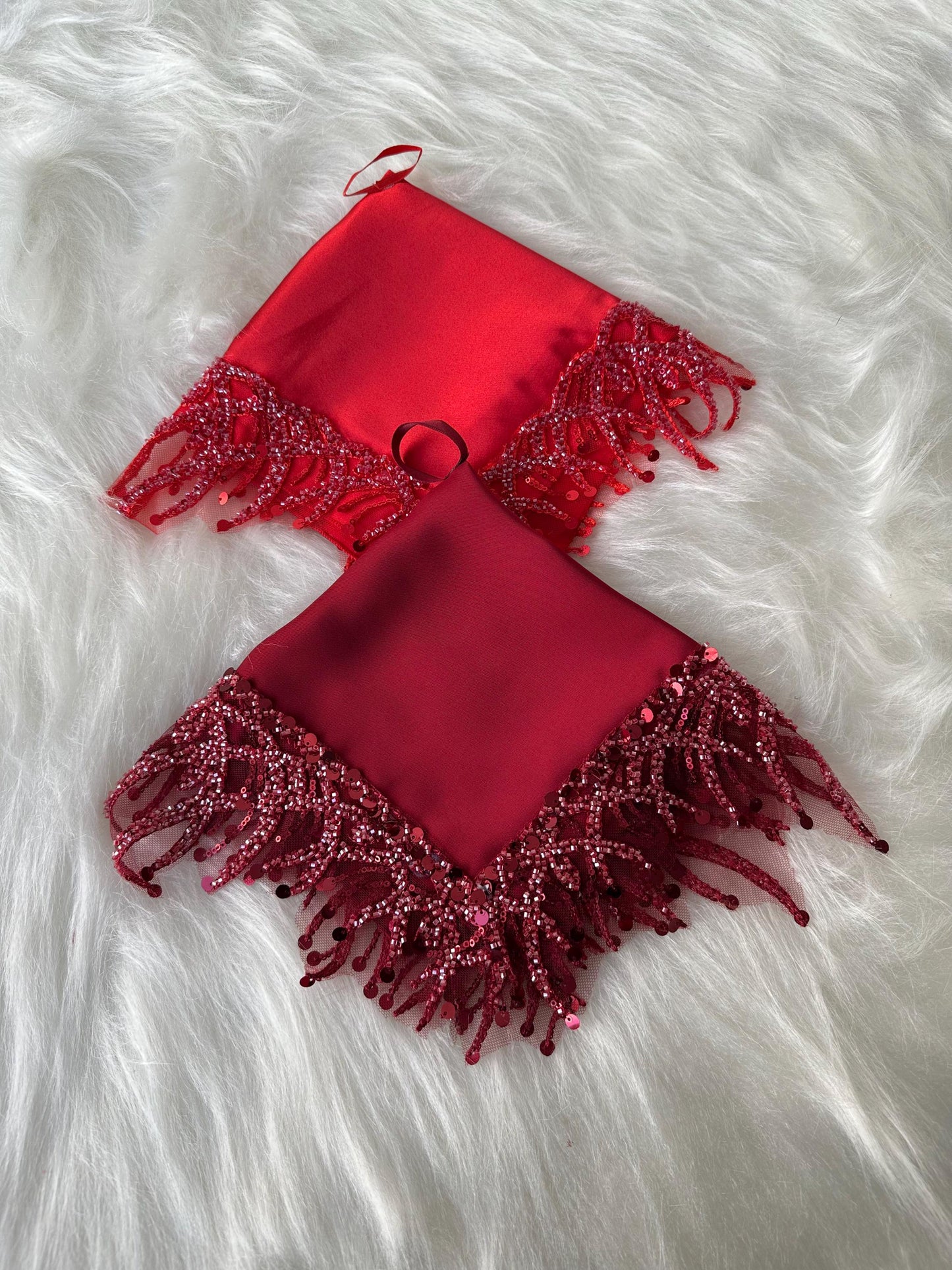 Two red satin square scarves with sequined trim and fringe. The scarves are on a white fuzzy surface.