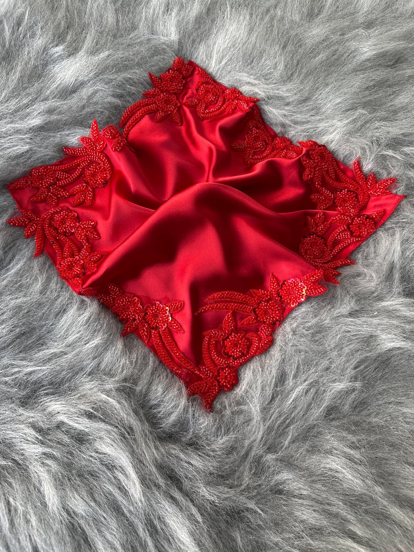 A red satin square with a red beaded floral design around the edges