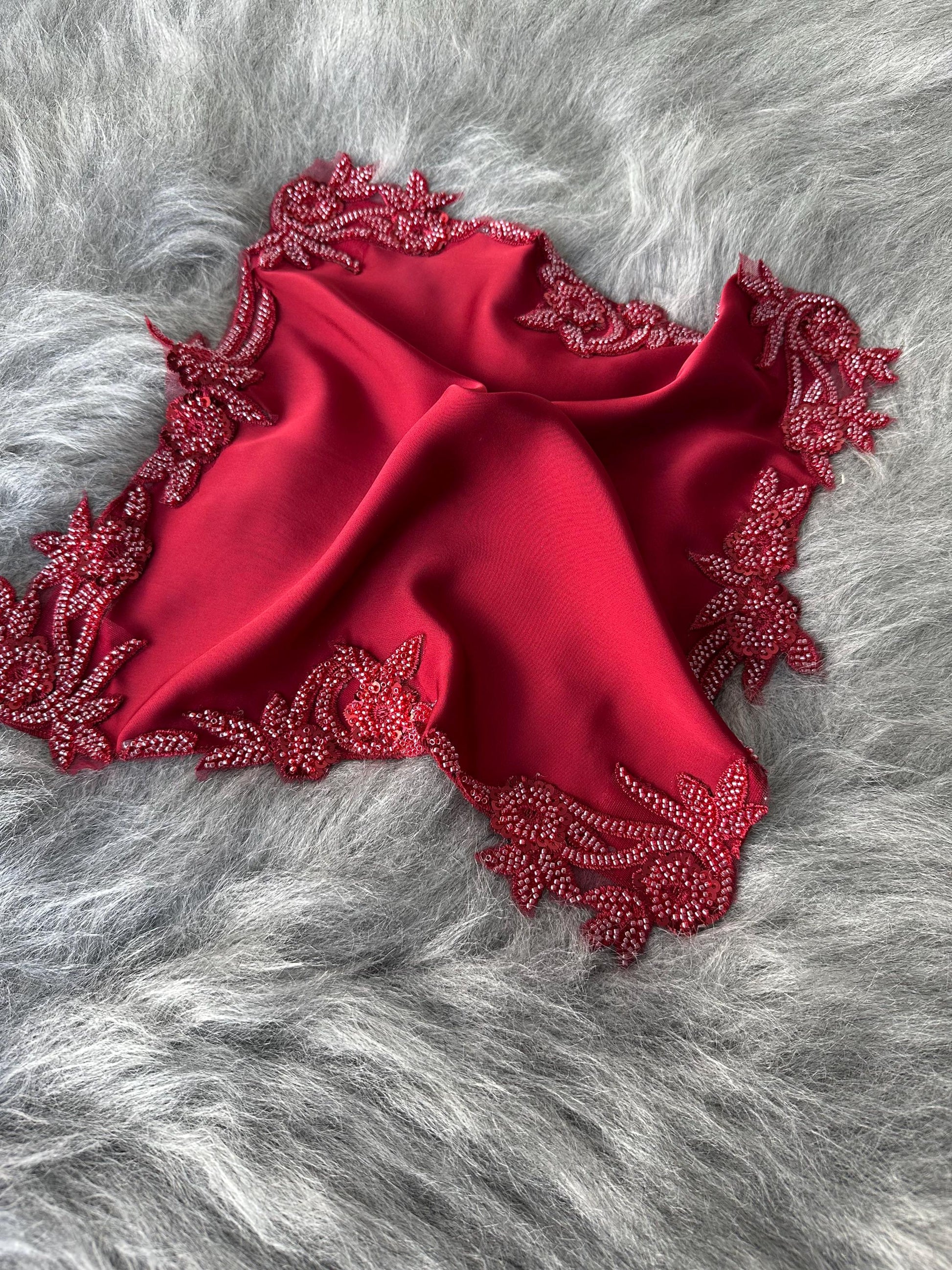 A red satin scarf with a beaded floral design around the edges.