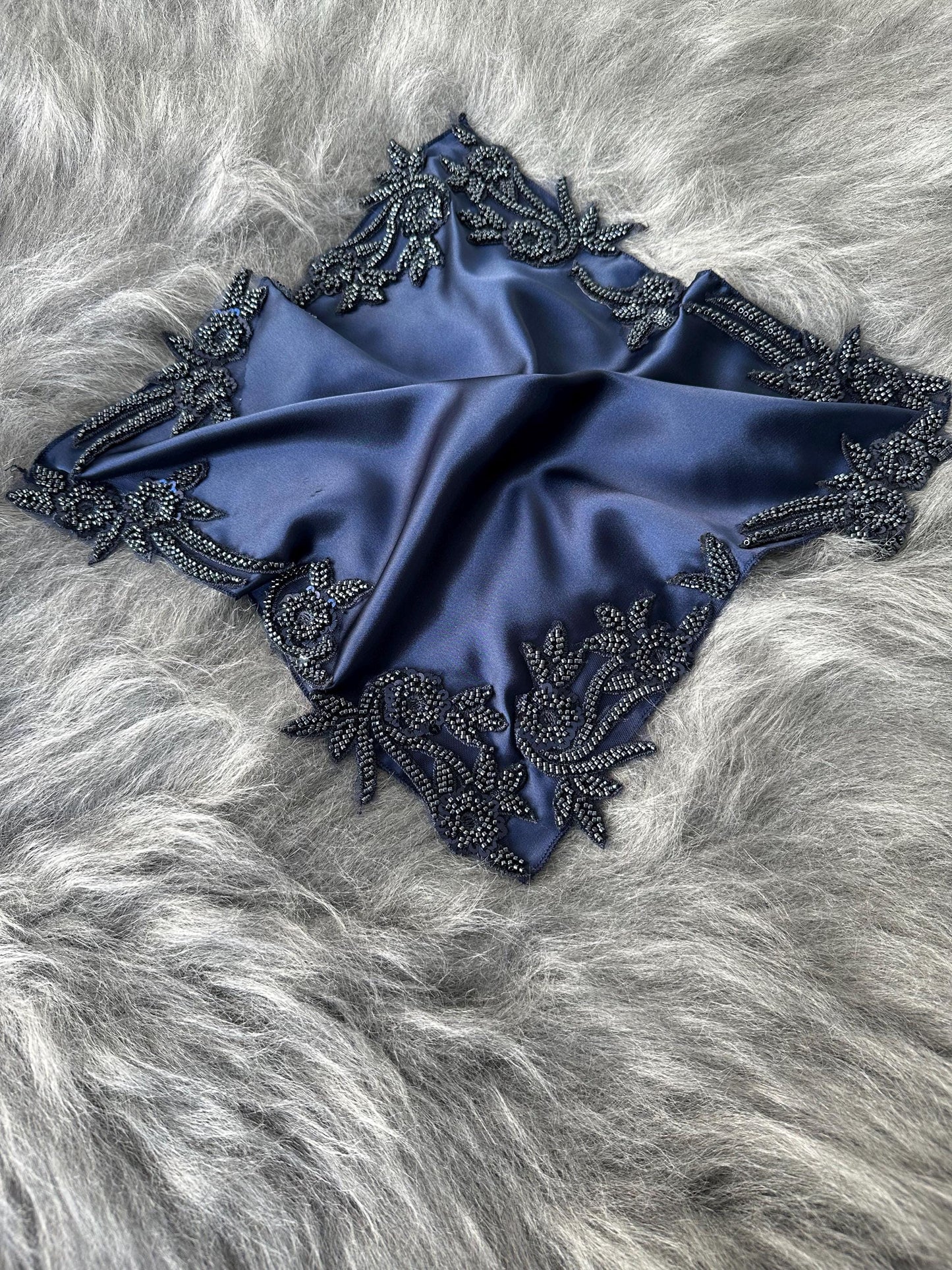 A dark blue satin scarf with a black beaded floral design around the edges.