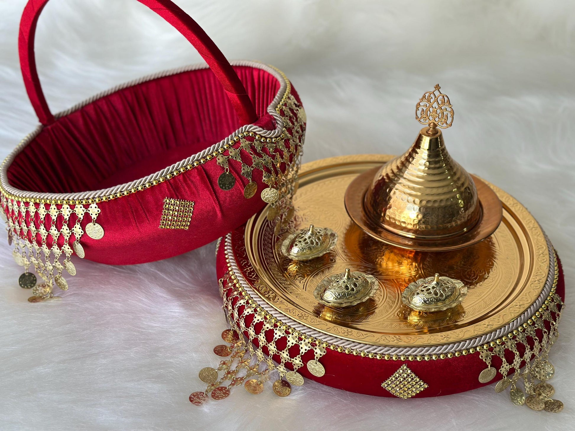 A red velvet tray with gold trim and a gold metal tray with a gold metal lid and decorative accents. The trays are decorated with gold coins and tassels. The trays are used for a traditional Turkish wedding ceremony.