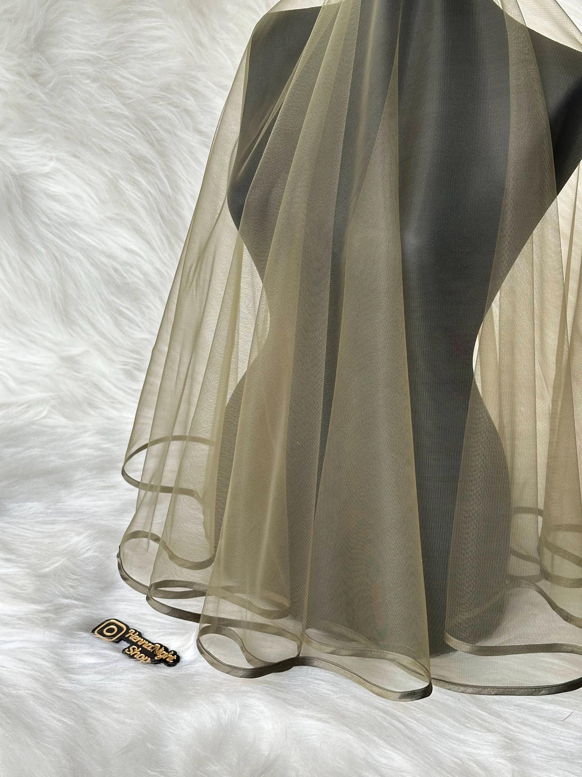 A sheer, light green fabric with a dark green trim. The fabric is draped over a mannequin and has a wavy edge.