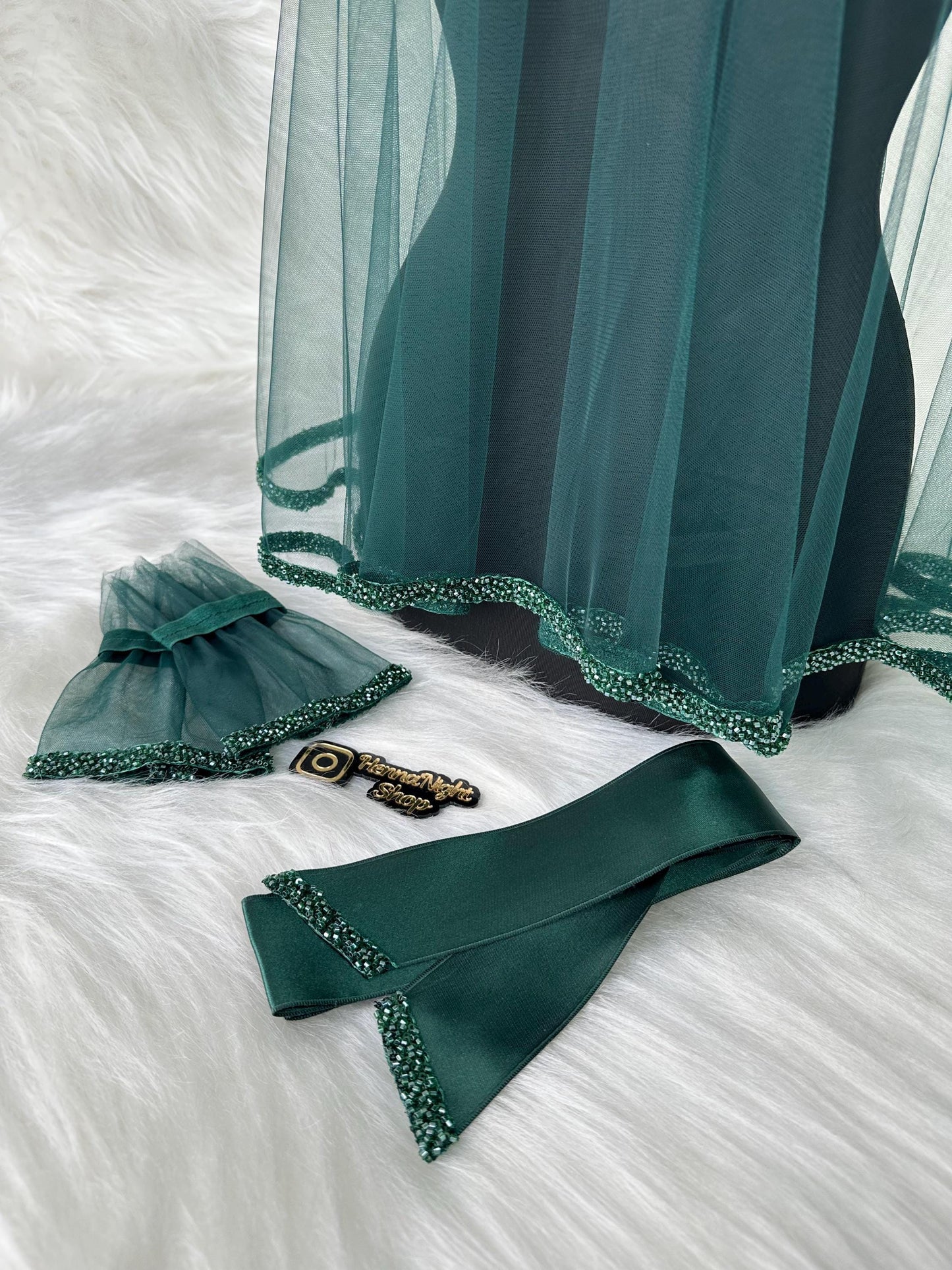 A green tulle veil with a beaded trim, a green satin sash with a beaded trim, and a pair of green tulle wrist cuffs with beaded trim.