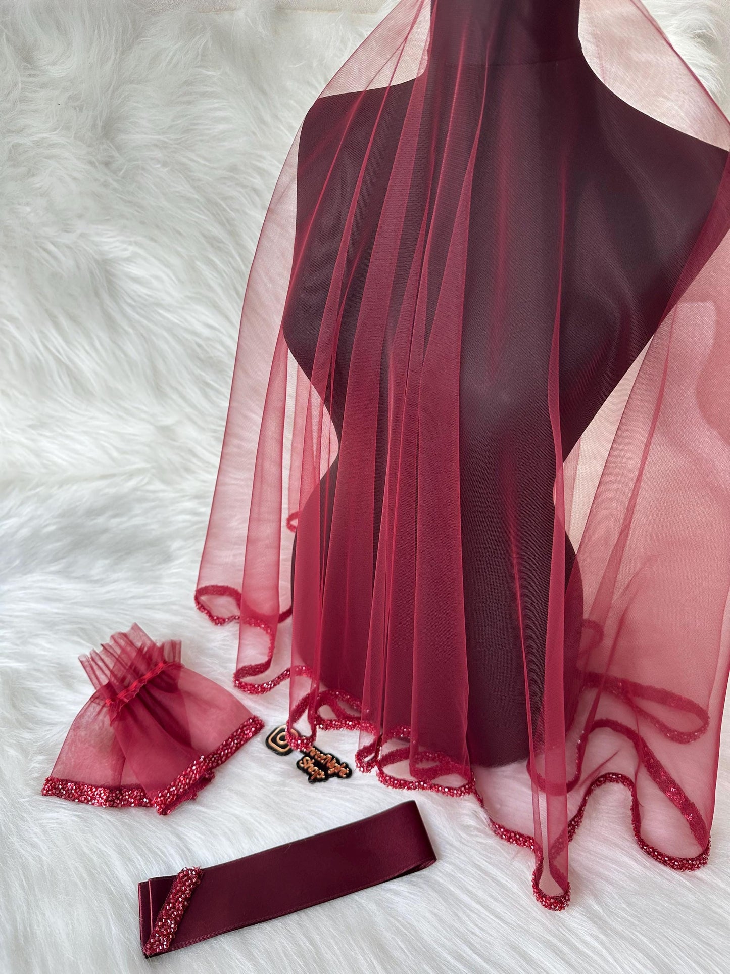 : A burgundy tulle veil with a beaded trim, a burgundy satin ribbon, and a pair of burgundy tulle wrist cuffs with beaded trim.