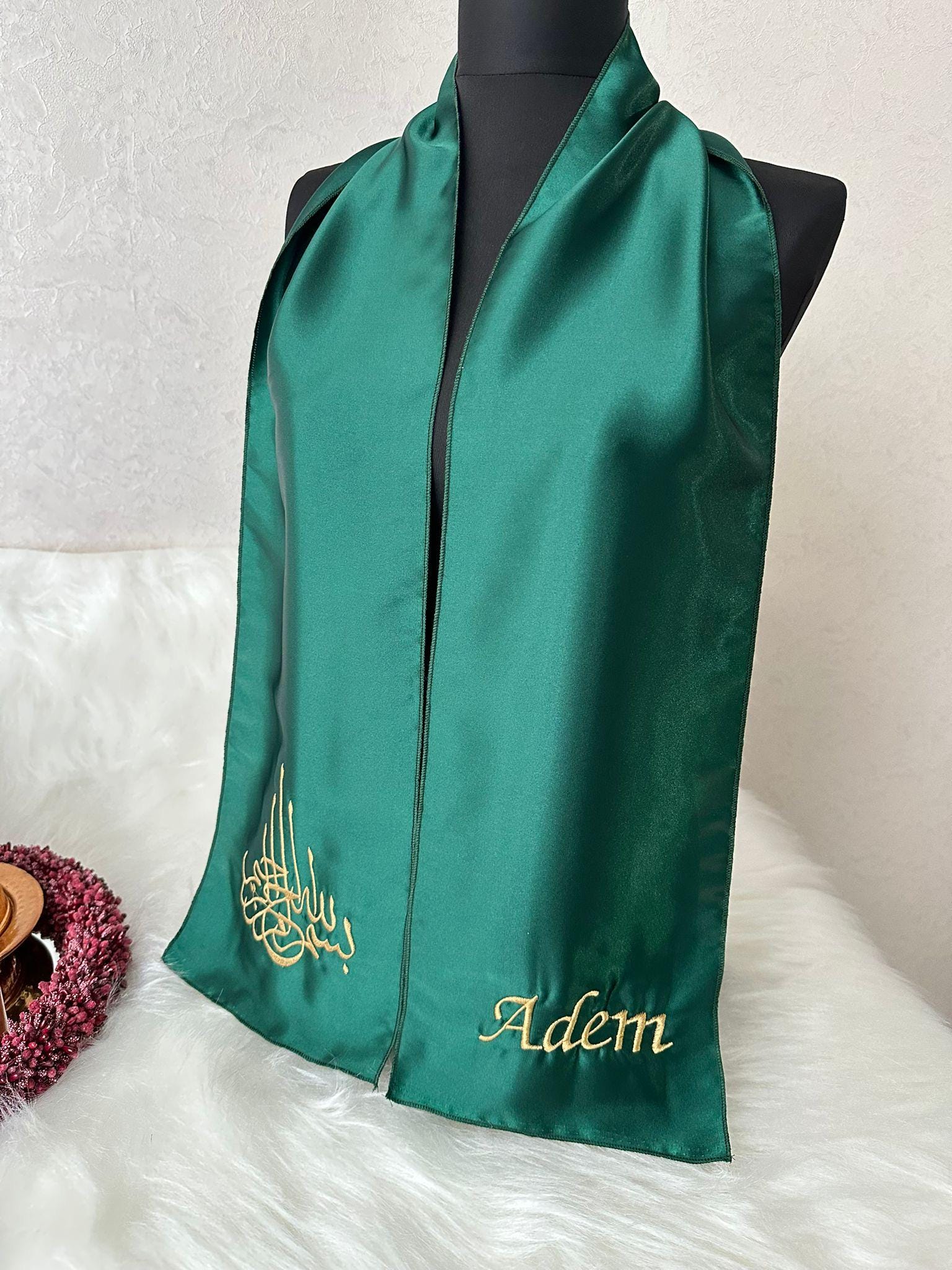 A dark green satin scarf with gold embroidery. The embroidery includes the Arabic word for 'Allah' and the name 'Adem'.