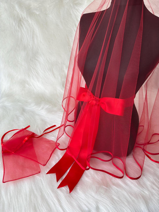 A red tulle veil with a red satin ribbon tied around the center. The veil has a scalloped edge and is displayed on a mannequin. There is also a small red tulle bag with a red satin ribbon.