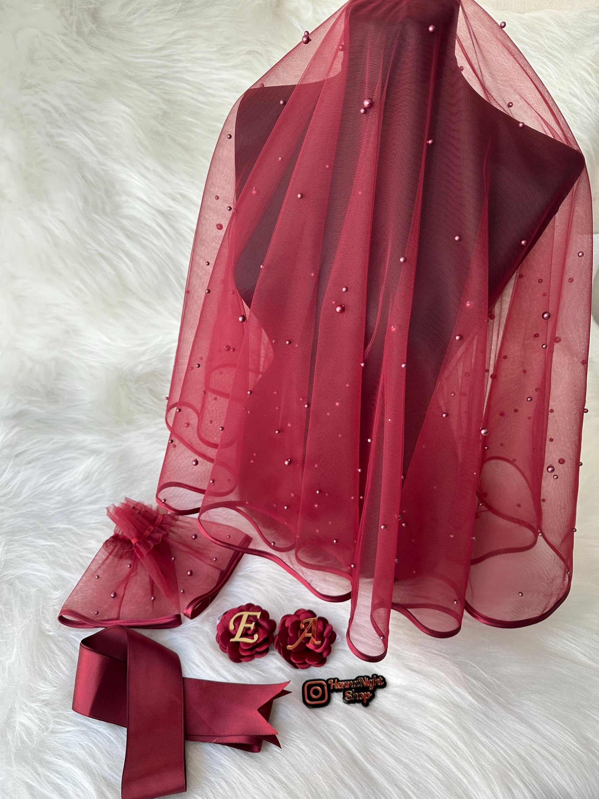 henna A burgundy bridal veil with pearl embellishments, a burgundy satin ribbon, a pair of burgundy tulle wrist cuffs with pearl embellishments, and two burgundy fabric flower brooches with gold letter accents. The brooches spell out 'EA'. The image also includes a small square sticker with the text 'Happy Wife Shop' and an Instagram logo.