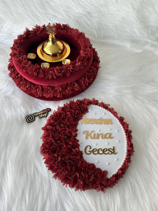 A white round tray with a red fabric border decorated with red fabric flowers. The tray has gold lettering that reads 'Asena'nin Kina Gecesi'.