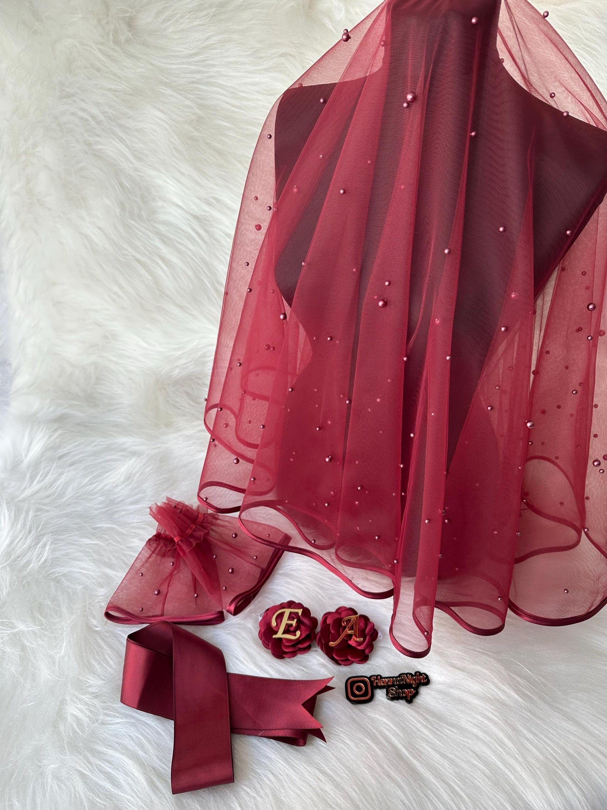 A burgundy tulle veil with pearl embellishments, a burgundy satin ribbon, two burgundy fabric flowers with gold letters spelling 'EA', and a small burgundy and gold sticker with the text 'Flower Night Shop' and an Instagram logo.