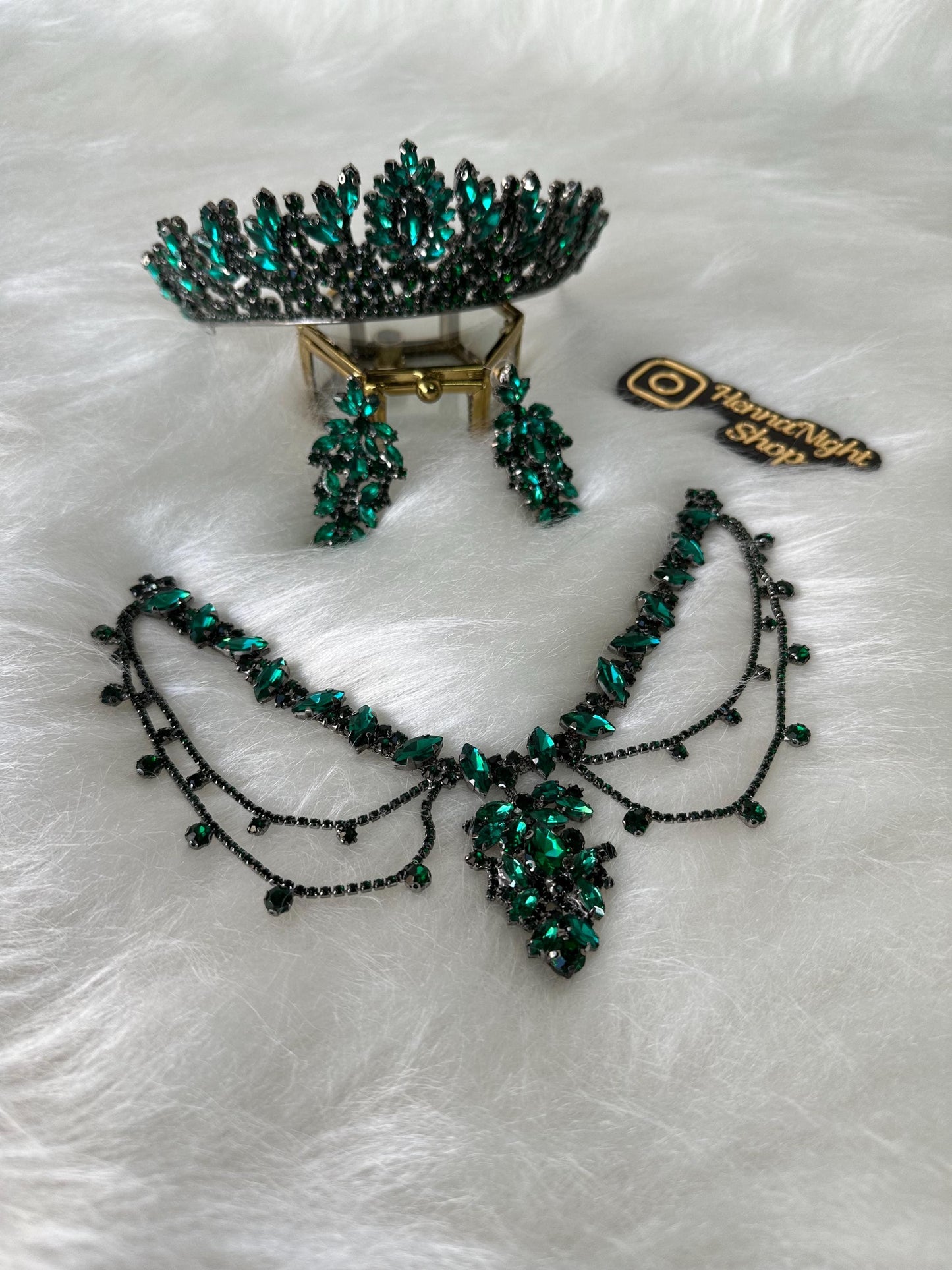 A green emerald crystal tiara, necklace, and earrings jewelry set. The tiara has a pointed crown shape with a row of emerald crystals. The necklace has a v-shaped design with a cluster of emerald crystals. The earrings are long and dangle with emerald crystals.