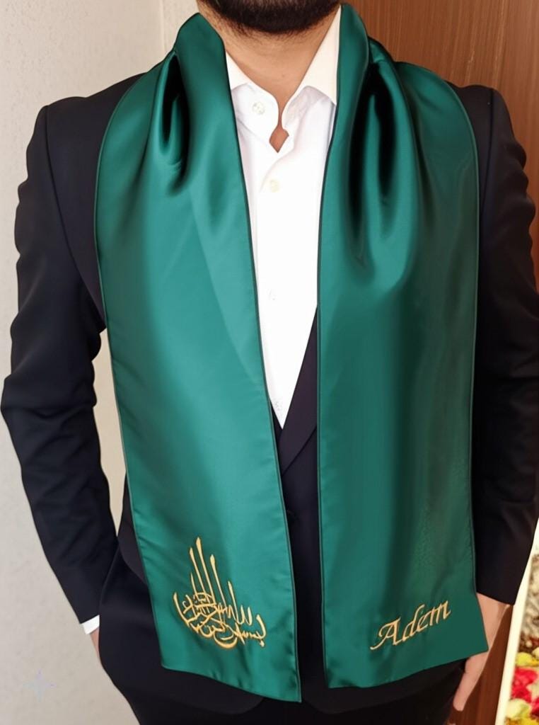 A dark green satin scarf with gold embroidery. The embroidery includes the Arabic word for 'Allah' and the name 'Adem'.
