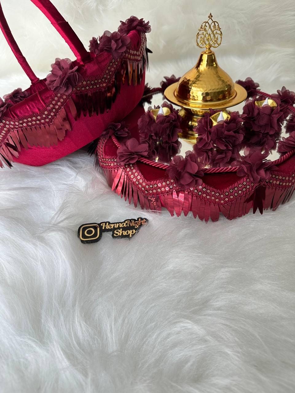 henna Two decorative trays with gold accents and red velvet fabric. The trays are adorned with burgundy fabric flowers and gold sequins. The trays are on a white furry surface. The text 'Henna Night Shop' is visible in the lower left corner of the image.