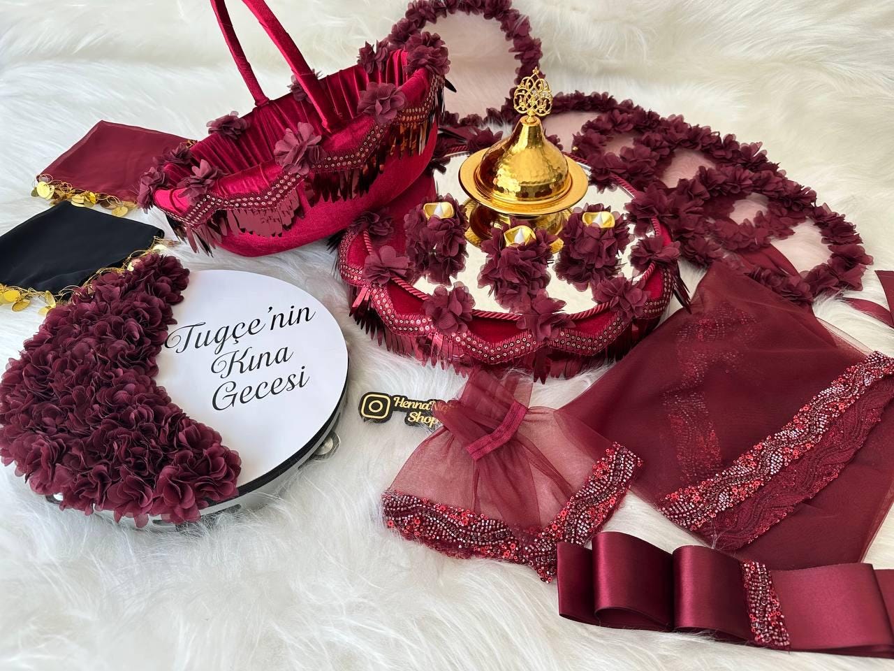henna A burgundy and gold henna night set with a tray, a basket, a decorative plate, a veil, and a ribbon. The tray has a gold bowl with a lid and is decorated with burgundy flowers. The basket is made of burgundy velvet and is decorated with burgundy flowers. The decorative plate is white with a burgundy border and is decorated with burgundy flowers. The veil is made of burgundy tulle and is decorated with burgundy beads. The ribbon is made of burgundy satin