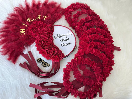 A red feather fan with the word 'MIRAY' in gold lettering. A white round plate with the text 'Miray'in Kına Gecesi' in black lettering. A set of red flower wreaths with gold accents.