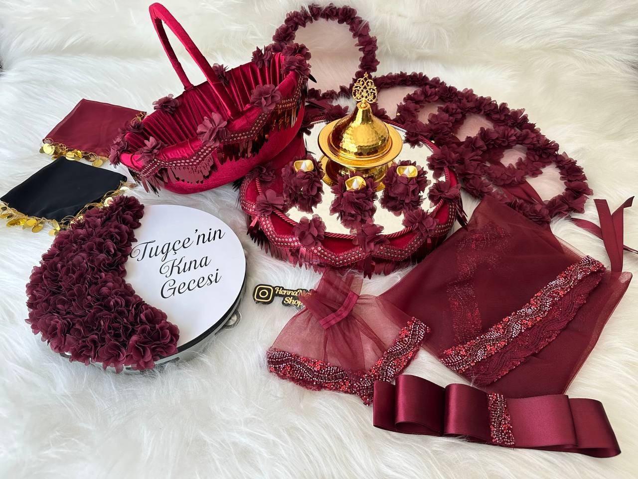 A burgundy and gold henna night tray set with a round tray decorated with burgundy flowers, a gold bowl with a lid, and a white plate with the words 'Tugcee'nin Kına Gecesi' in black text. The set also includes a burgundy velvet basket with a handle, a burgundy satin ribbon, and a burgundy tulle veil with a beaded edge.