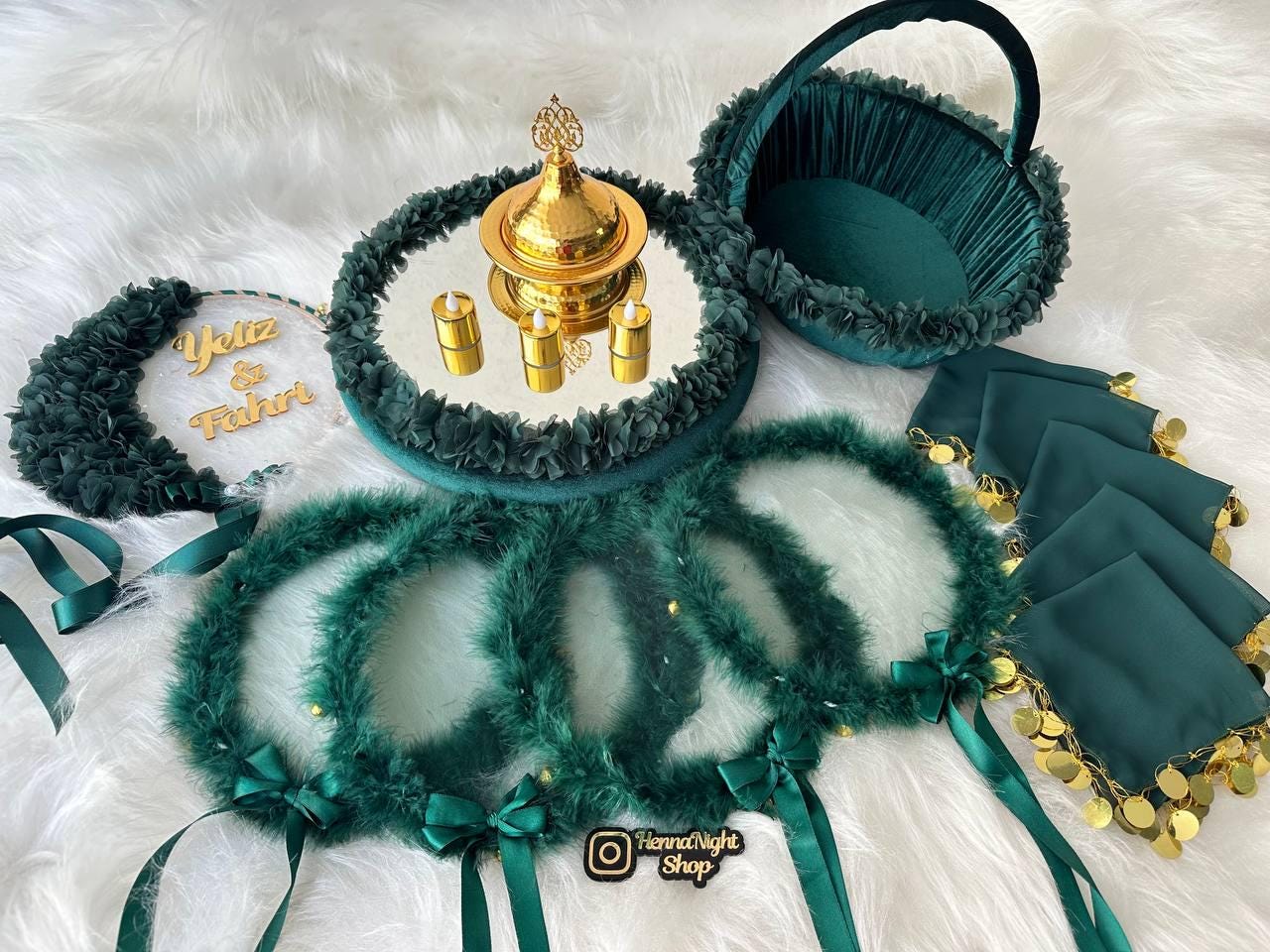 A white round sign with the text 'Tuğçe nin Kına Gecesi' in gold lettering. The sign is surrounded by green feathers, green beads, and green fabric. The sign is decorated with a red satin ribbon. The sign is on a white surface. henna tray and henna basket green